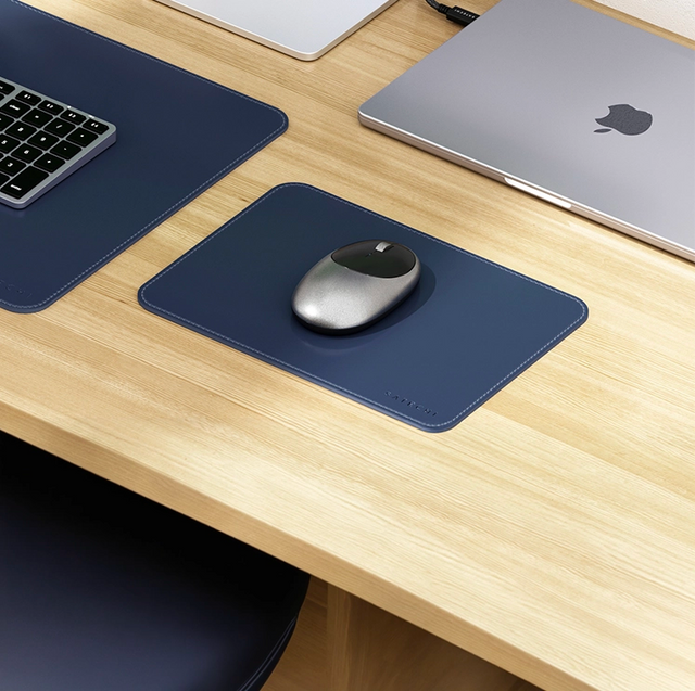 Satechi vegan leather mouse pad in navy on a wooden desk with a space gray M1 wireless mouse, next to a matching desk mat, keyboard and laptop.