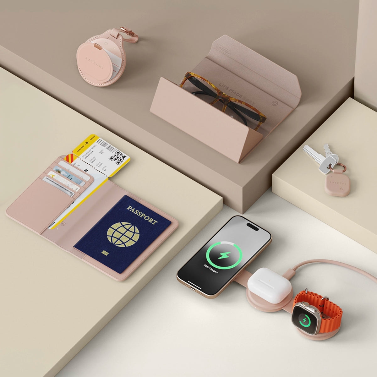 Satechi travel tech accessories in Desert Rose: the Vegan-Leather FindAll™ Passport Cover holding a passport and boarding pass, the Vegan-Leather FindAll™ Glasses Case with sunglasses inside, the Vegan-Leather FindAll™ Keychain on a set of keys, and the OntheGo™ 3-in-1 Charger wirelessly charging an iPhone, AirPods and an Apple Watch, all arranged on a cream and taupe backdrop.