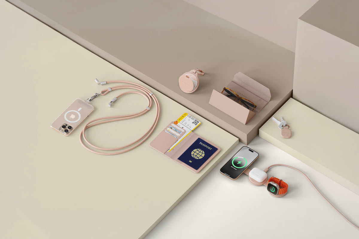 Satechi travel tech accessories in Desert Rose: the OntheGo™ USB-C Lanyard Cable attached to an iPhone in a clear MagSafe case, the Vegan-Leather FindAll™ Passport Cover holding a passport and boarding pass, the Vegan-Leather FindAll™ Glasses Case with sunglasses inside, the Vegan-Leather FindAll™ Keychain on a set of keys, and the OntheGo™ 3-in-1 Charger wirelessly charging an iPhone, AirPods and an Apple Watch, all arranged on a cream and taupe backdrop.