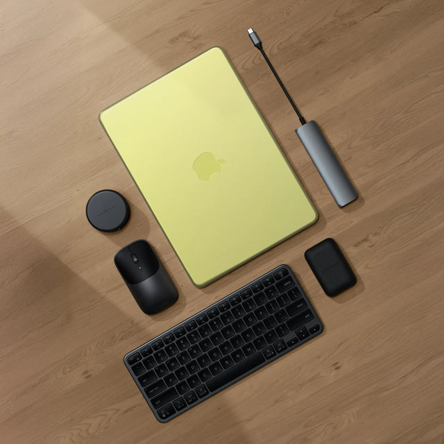 Top-down view of a Satechi workspace featuring a MacBook Neo on a light wood floor with a Satechi Slim EX1 Wireless Keyboard in dark, Slim EX Wireless Mouse, 7-in-1 USB-C Slim Multiport Adapter with Ethernet, and OntheGo™ 7-in-1 Multiport Adapter — best MacBook Neo accessories 2026