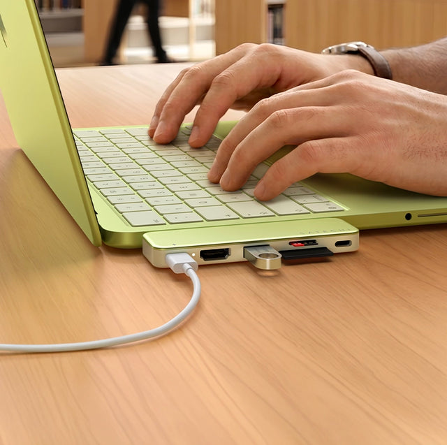 Citrus  Satechi slim USB-C Snap Hub hub plugged into a citrus MacBook Neo, with a USB-C cable, USB flash drive and SD card connected, as a person types.