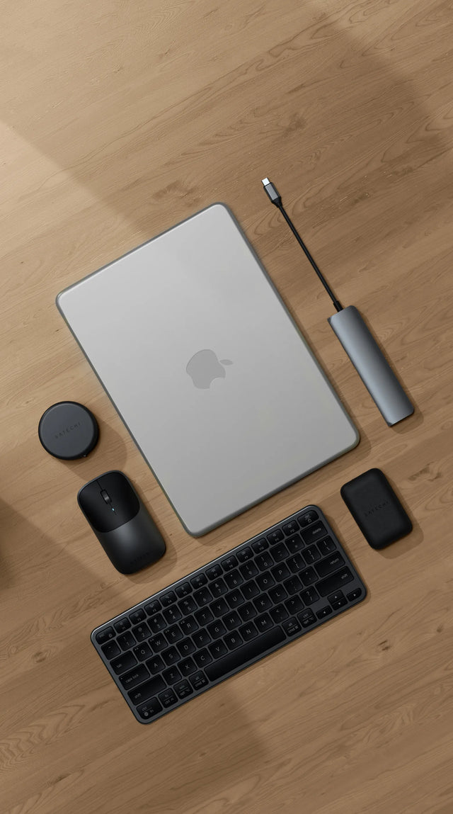 Top-down view of a Satechi workspace featuring a MacBook Pro M5 Pro / Max on a light wood floor with a Satechi Slim EX1 Wireless Keyboard in dark, Slim EX Wireless Mouse, 7-in-1 USB-C Slim Multiport Adapter with Ethernet, and OntheGo™ 7-in-1 Multiport Adapter — besta MacBook Pro M5 Pro accessories 2026