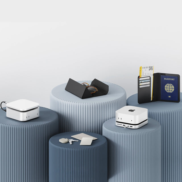 Satechi premium tech and travel accessories arranged on display pedestals, including USB4 Slim NVMe SSD Enclosure, Mac Mini M4 Stand & Hub with SSD Enclosure, FindAll smart tracking card, Vegan-Leather FindAll Keychain, Glasses Case, and Passport Cover for storage, organization, and Apple-compatible device setups.