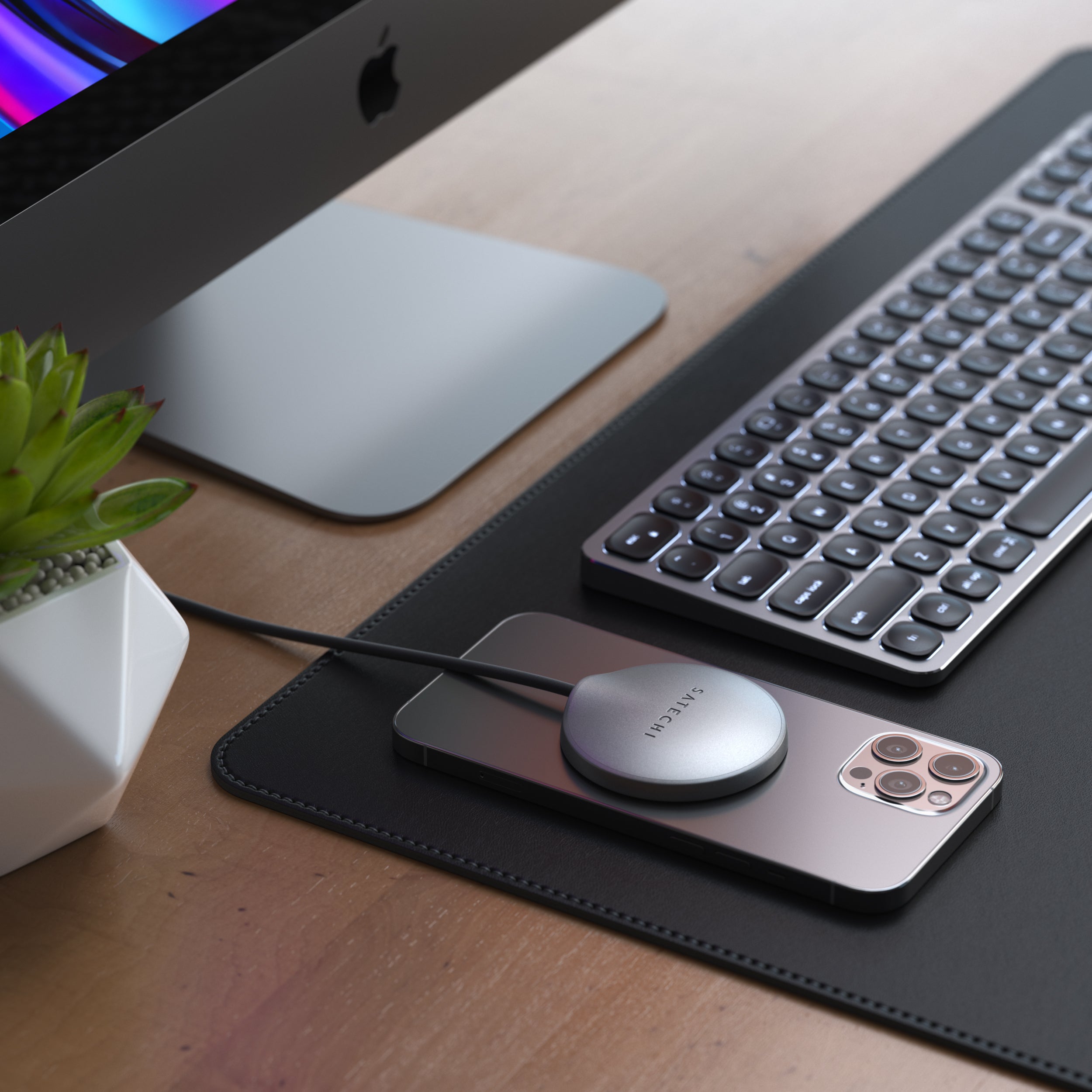 An iPhone  on a desk being charged by USB-C Magnetic Wireless Charging Cable with keyboard and computer monitor in the background.