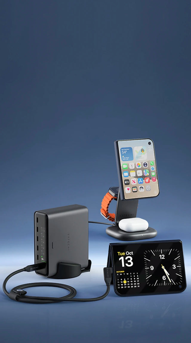 Desktop charging setup for iPhone Duo in a row from left to right: the Satechi ChargeView™ 240W Desktop Charger, an iPhone Duo folded into tent mode showing a clock and calendar for Tuesday, October 13 and connected with the Right-Angle USB-C to USB-C Data and Charge Cable (1m), and a closed iPhone Duo charging on the the 3-in-1 Foldable Wireless Charging Stand with Qi2 25W. An Apple Watch with an orange band and AirPods in their case sit on the other charging platforms.