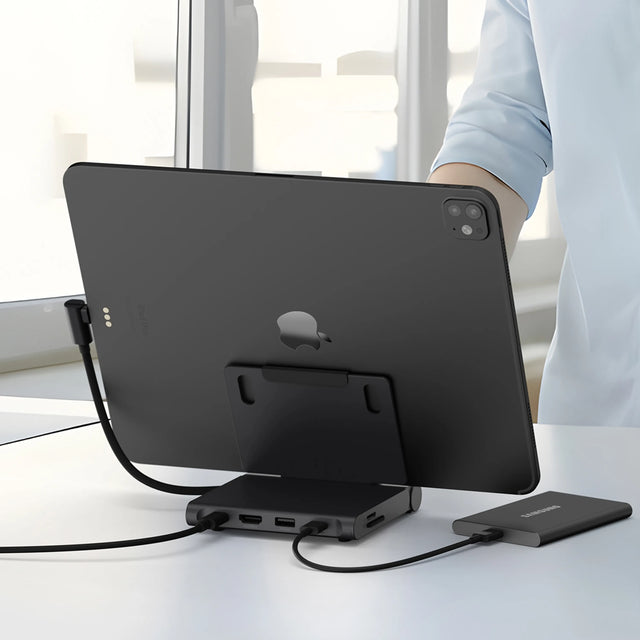 iPad connected to the Satechi OntheGo™ Foldable Stand Hub on a desk, with the hub’s USB‑C and data ports visible while a person uploads files from an external SSD drive.