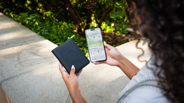 O persoană care ține o husă de pașaport din piele vegană FindAll™ în timp ce un iPhone monitorizează activ cu tehnologia Apple Find My.
