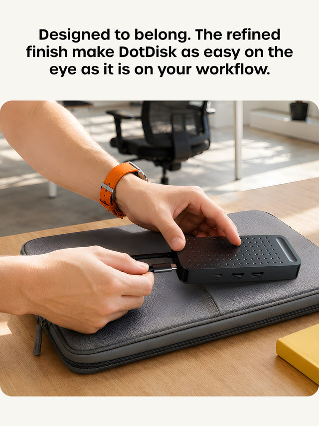 Designed to belong. The refined finish make DotDisk as easy on the eye as it is on your workflow. Hands tuck the host cable of the Space Black ExtendView USB4 hub into its built-in cable slot on a gray laptop sleeve.