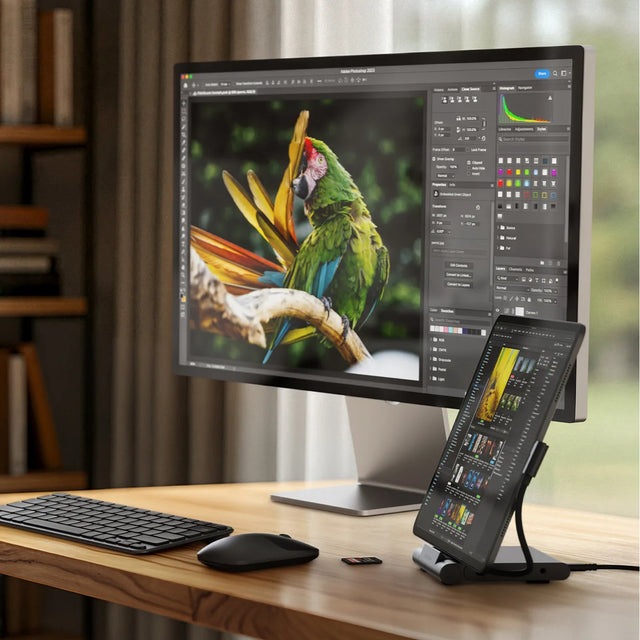 Desktop workspace with an iPad mounted on the Satechi OntheGo™ Foldable Stand Hub and connected to a large external monitor displaying photo‑editing software. A keyboard and mouse sit on the desk beside the hub.