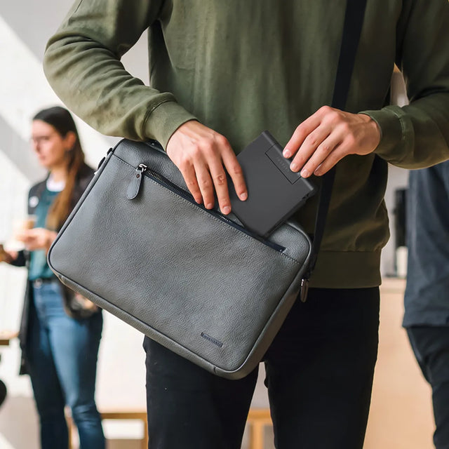 Person placing the folded Satechi OntheGo™ Foldable Stand Hub into the front pocket of a laptop bag, highlighting the hub’s compact, travel‑friendly design.