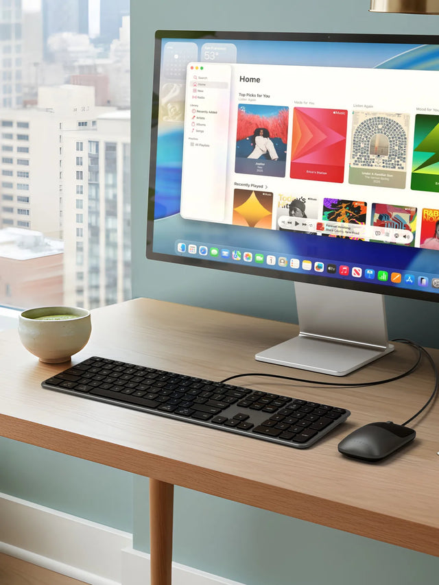 Slim LX3 Wired Keyboard and Slim LX Wired Mouse displayed on a modern wood desk setup with a widescreen monitor, showing a clean and minimalist workspace ideal for productivity. The ultra‑slim wired keyboard and mouse are positioned neatly beside a ceramic coffee cup and stacked books, highlighting a contemporary home office featuring natural light and desktop accessories.