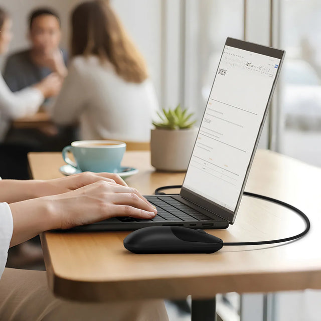 Person using a laptop and Slim LX Wired Mouse in a coffee shop.