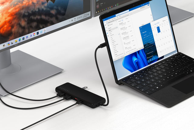 Adaptor multiport USB-in-1 USB-C Triple Display conectat la un laptop, cu mai multe cabluri HDMI și USB atașate, demonstrând ieșire multi-monitoare și conectivitate extinsă pentru o configurație desktop completă.